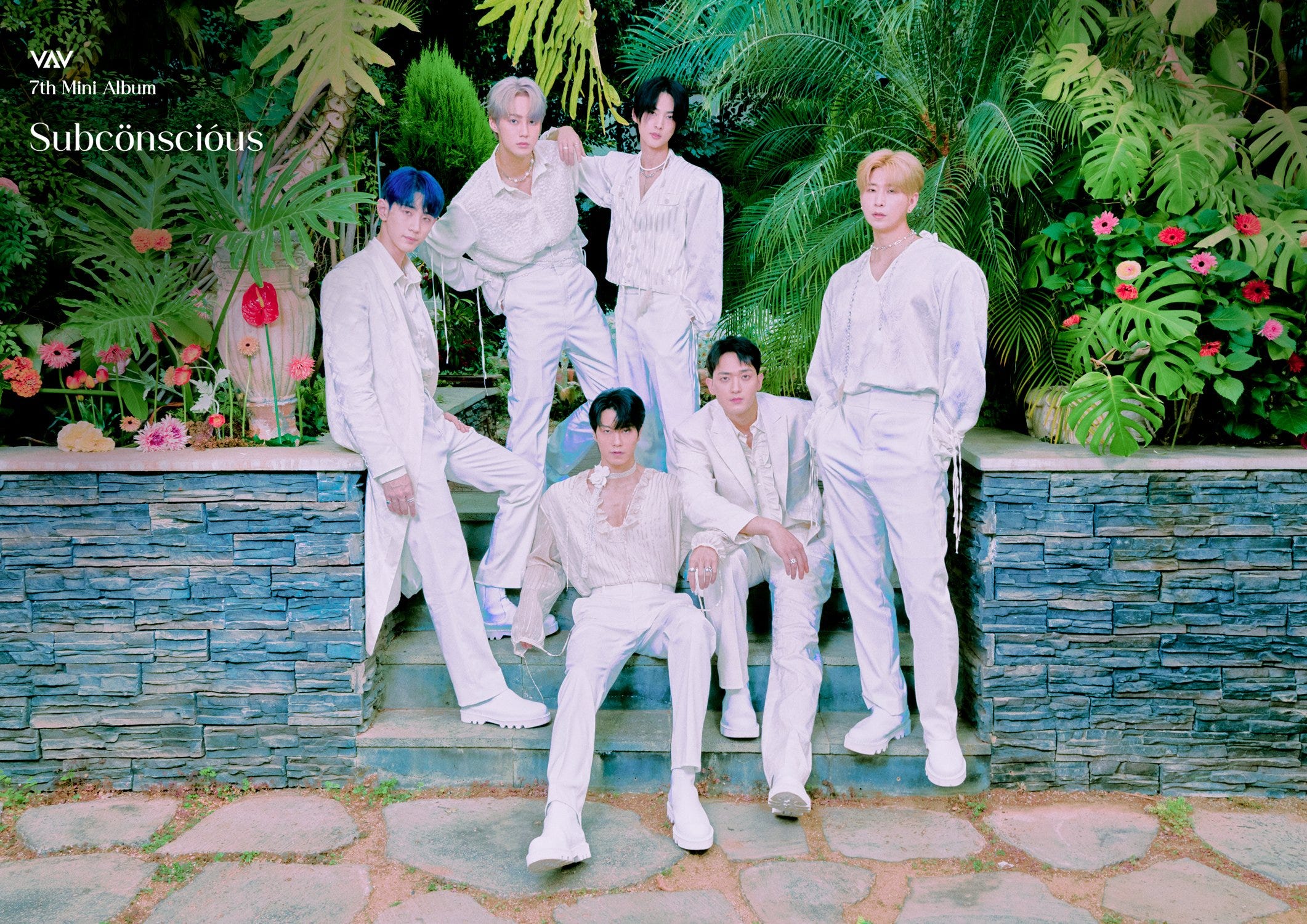 VAV promotional image, members posing on a blue brick wall surrounded by tropical foliage, wearing white outfits.