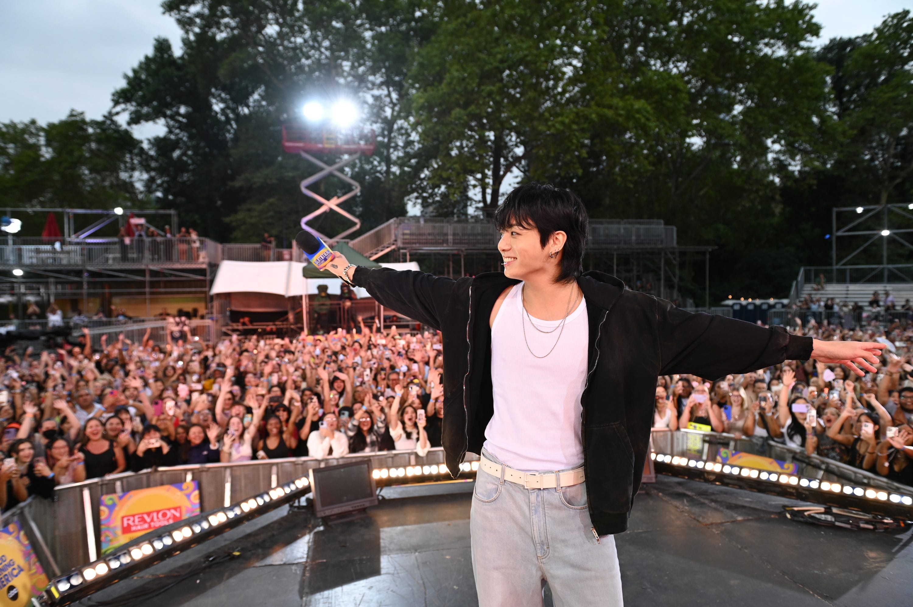 Jungkook posing on the GMA stage with his arms out, ARMY i nthe background cheering him on