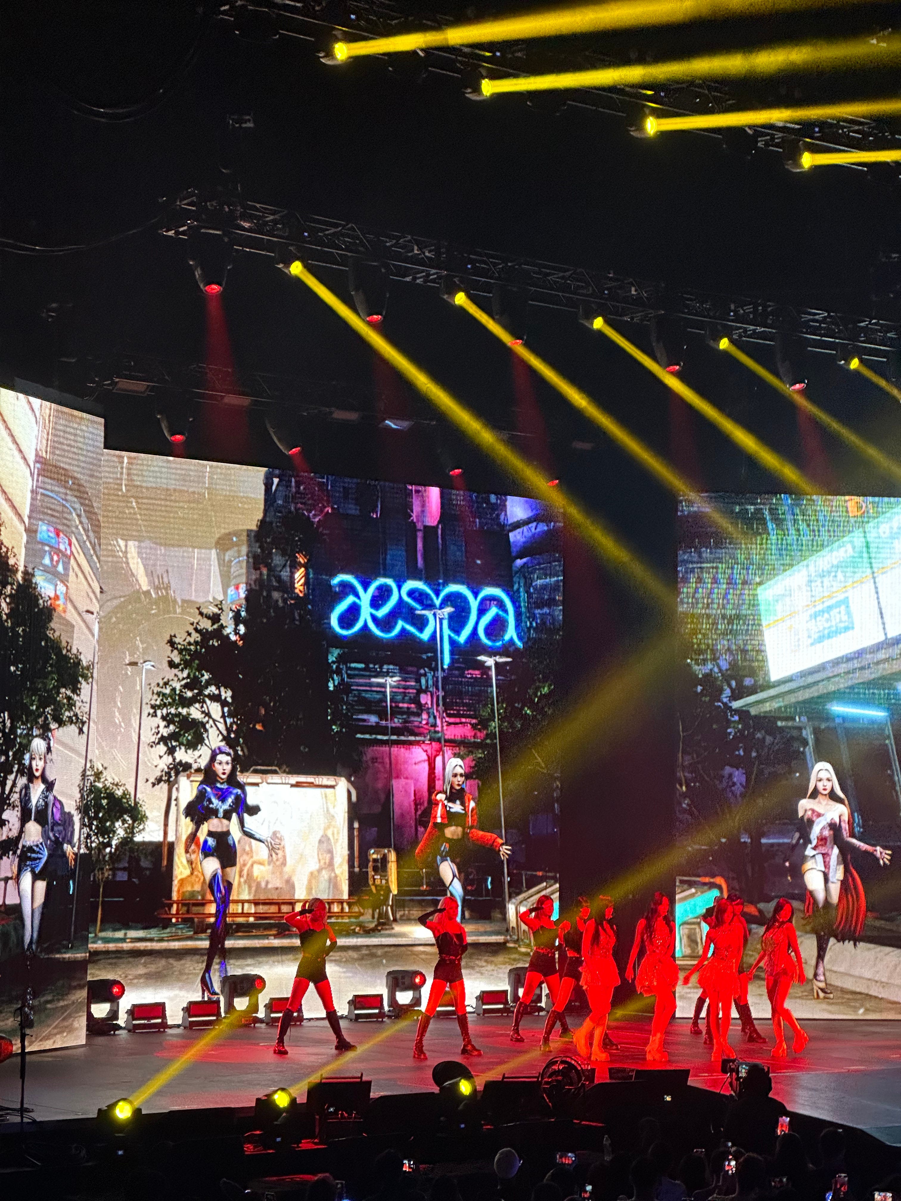 photo of aespa and their dancers performing on stage, wit their logo and ae's on screenbehind them