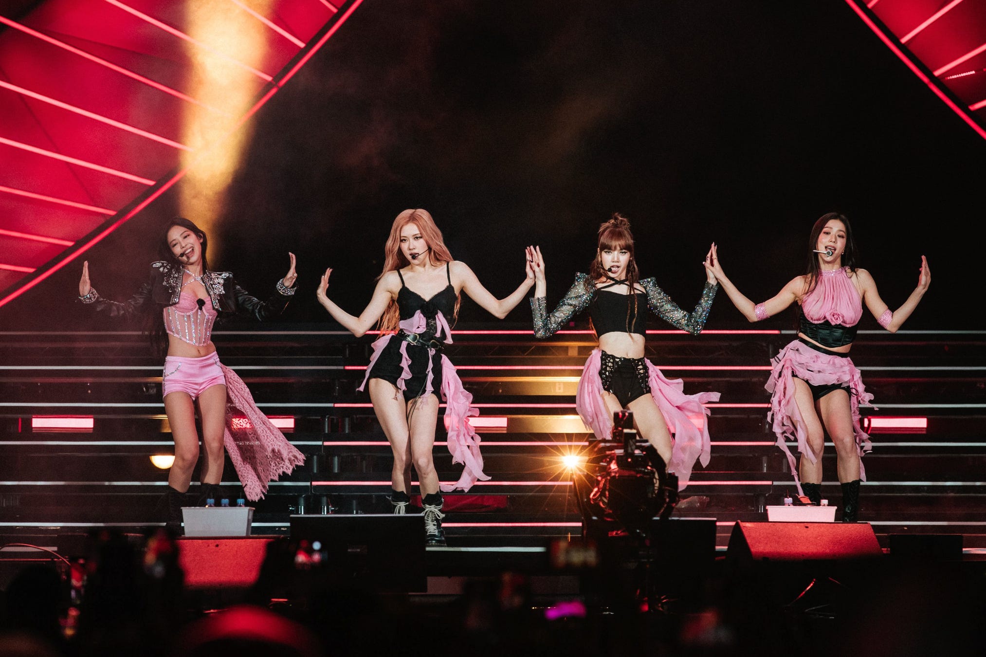 Blackpink performing at coachella. Jennie, Rosé, Lisa and Jisoo pose on stage with hands raised in pink, black, and silver looks