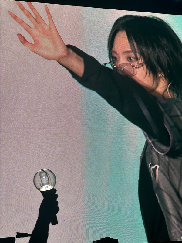 Seonghwa on-screen at Citifield, his arm covering the bottom of his face, with an Ateez lightstick raised in the corner