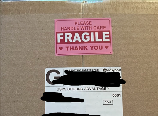 A package with a blacked-out USPS mailing label with "PLEASE HANDLE WITH CARE FRAGILE THANK YOU" sticker