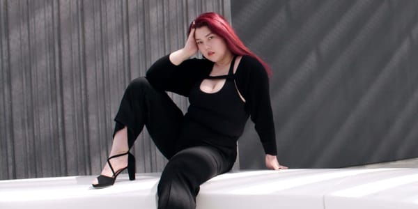 Isabel Jones posing against a gray wall, wearing all black. 