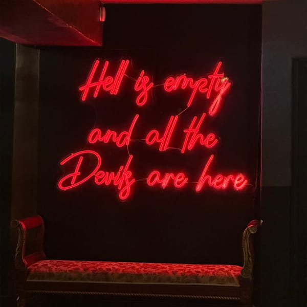 Red neon sign proclaiming "Hell is empty and all the Devils are here" above a red fabric bench.