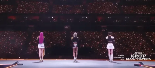 BabyMonster facing away from the camera on-stage, performing K-Pop Demon Hunters at MAMA with the words "Official Collaboration with NETFLIX K-POP DEMON HUNTERS"